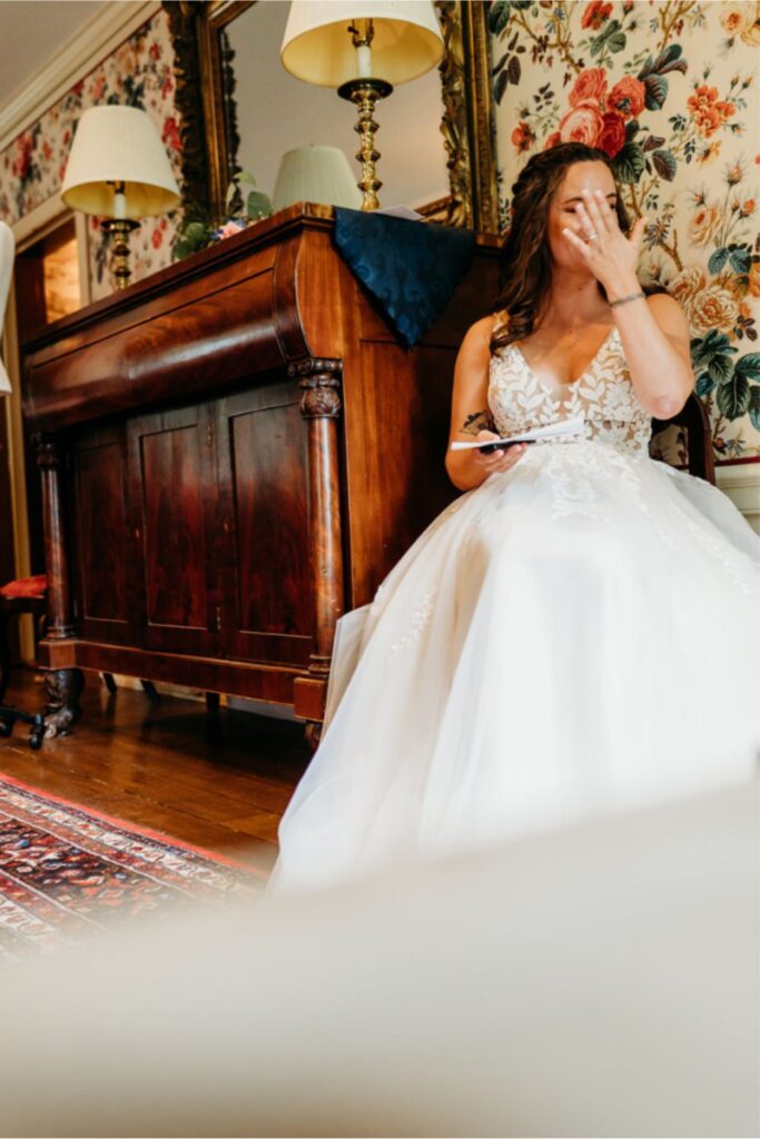 A bride seated, wiping away tears with a tissue while reading a heartfelt letter before her wedding ceremony.