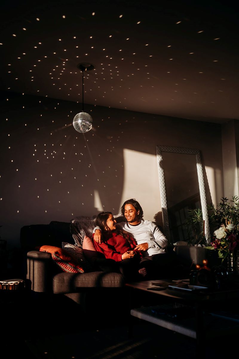 man and woman sitting together on a couch underneath a disco ball 