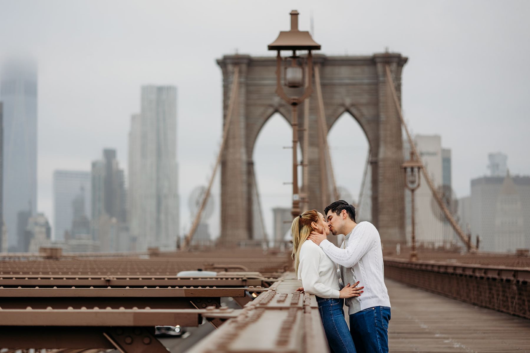 couple on the brooklyn bridge in new york the man is leaning in to give the woman a kiss 