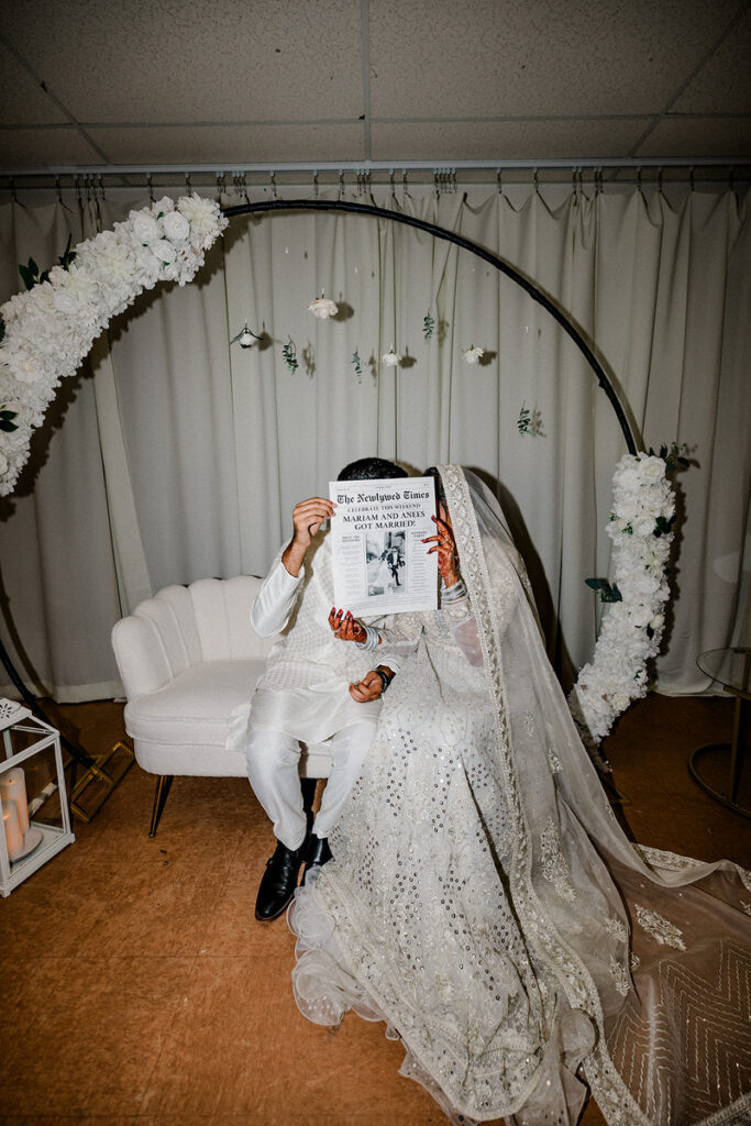 A newlywed couple holding up a custom newspaper over their faces 