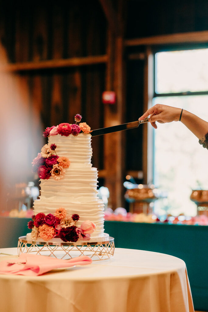 A hand cutting a three tiered wedding cake 