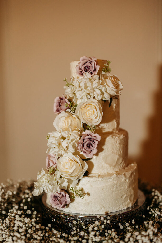 A four tiered wedding cake with flowers down one side 
