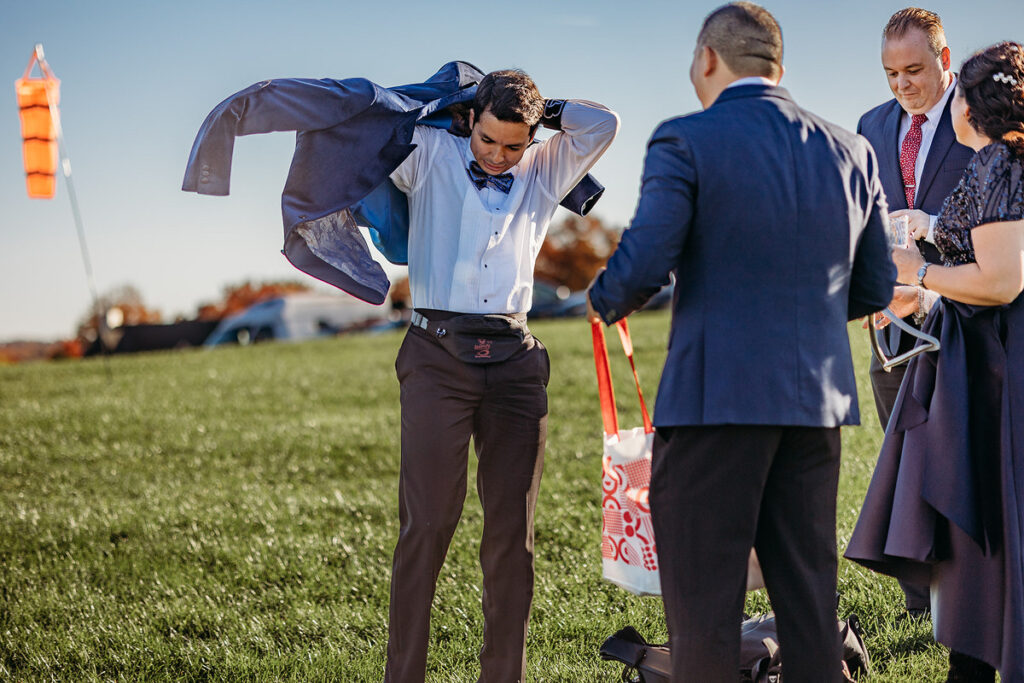 A groom putting on his wedding jacket with people standing around him 