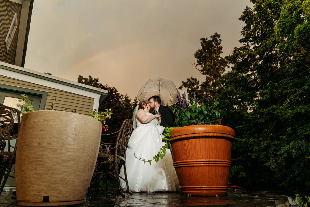 A couple kissing while standing on a small patio with a rainbow behind them 