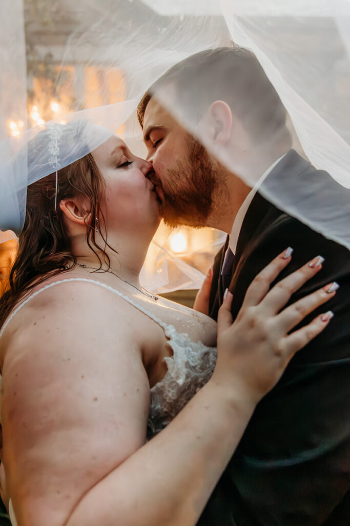 A newlywed couple kissing under a veil 