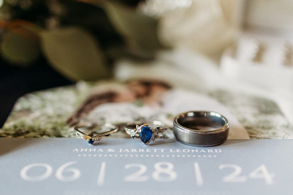 A close up of wedding rings laid on top of a wedding invitation 