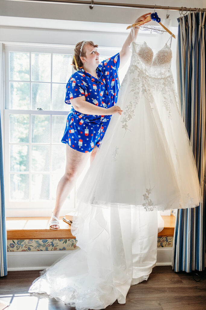 A person standing on a small alcove and grabbing a wedding dress from a curtain rod 
