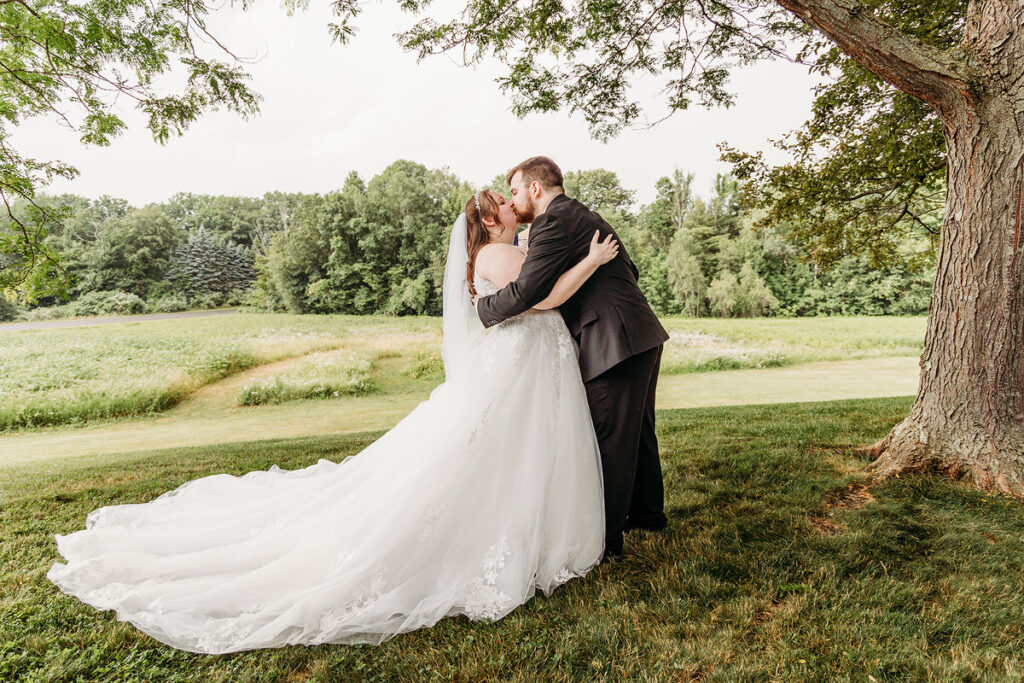 A newlywed couple kissing next to a tree 
