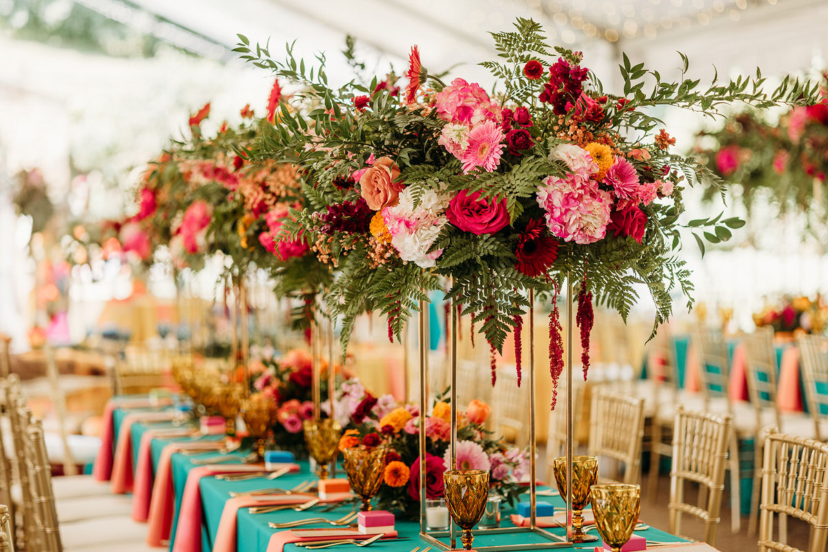 Colorful floral arrangements on a table with a blue table cloth and pink napkins showing predictions for 2025 destination wedding trends