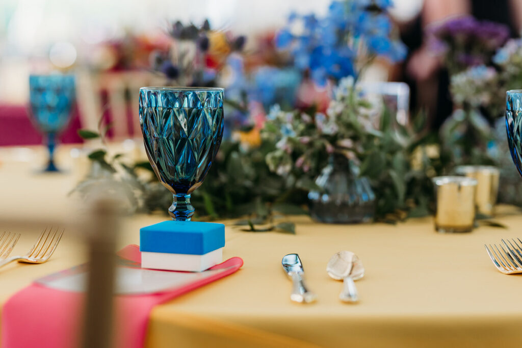 a colorful glass on a wedding reception table with flowers in the middle 