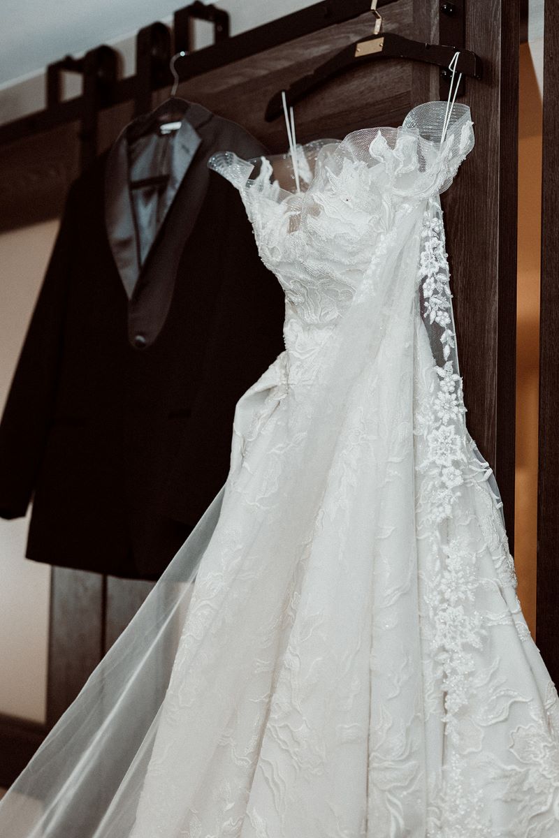 A white wedding dress on a hanger is handing up next to a black tuxedo top 