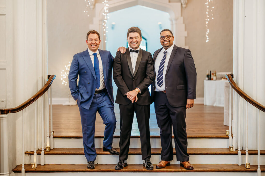 A groom smiling with two friends standing on either side 