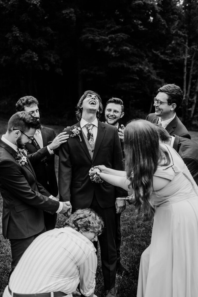 A groom laughing with friends standing around them smiling and adjusting their jacket  