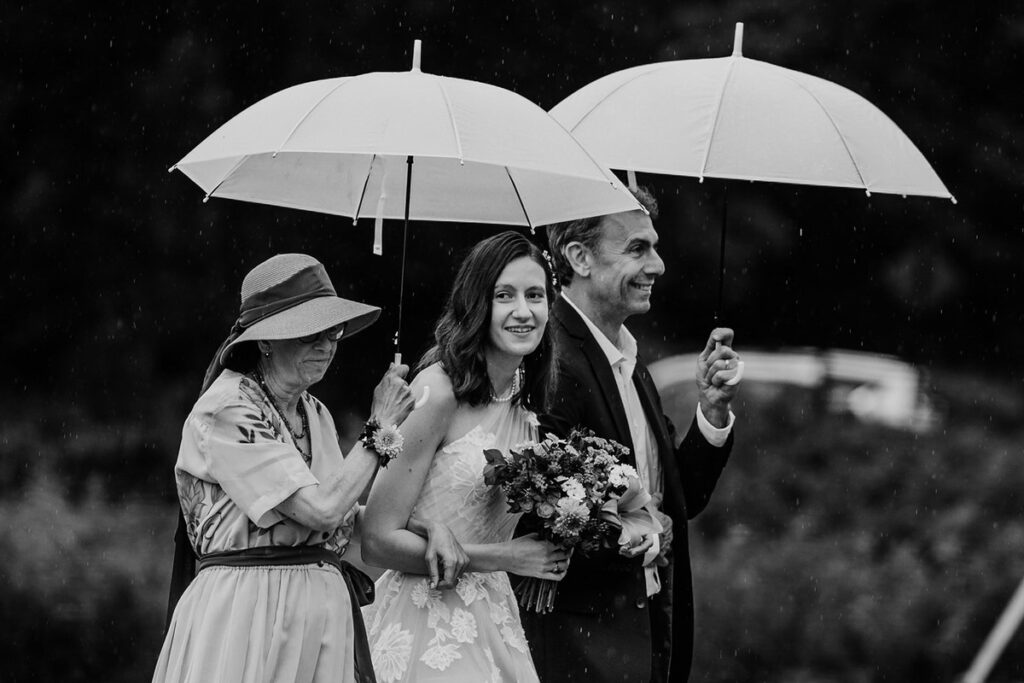 Parents walking their child down the aisle o their wedding day while holding umbrellas 