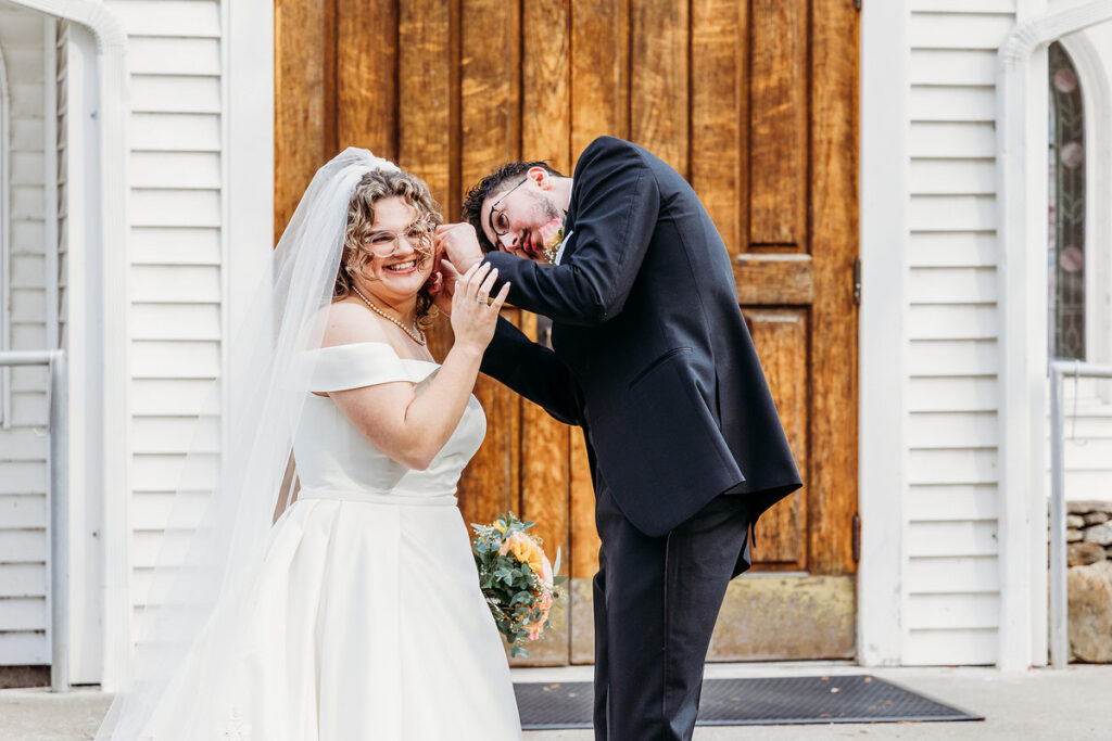 A person smiling and adjusting their partner's earrings on their wedding day 