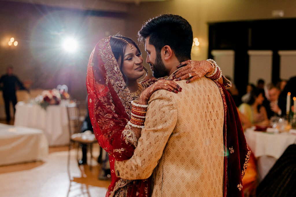 A newlywed couple with their arms close around each other dancing at their wedding 