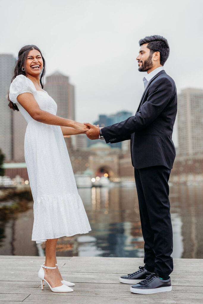 A couple holding hands and laughing together while standing on a pier 