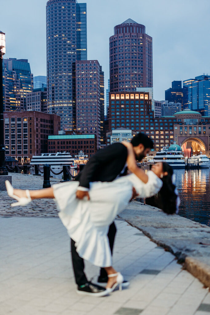 A person dipping their partner at dusk with a city skyline behind them 