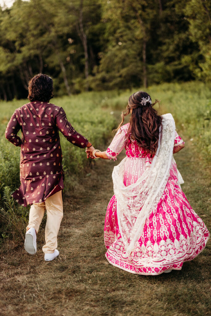 A newlywed couple holding hands and running through a field 